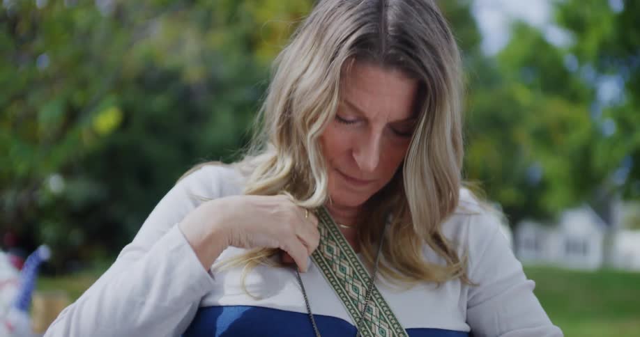 Close up of a middle aged woman inspecting a neck jewelry piece while standing outdoors during daytime