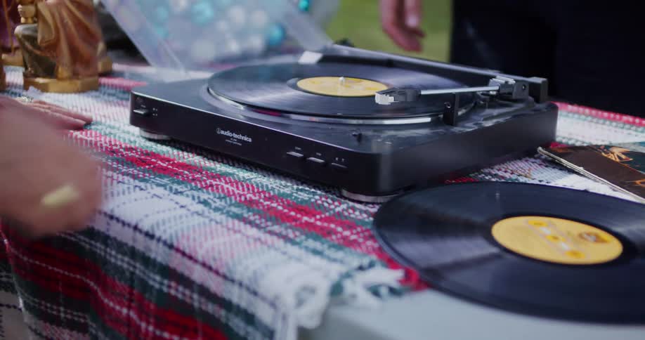 Hands position a record player on a table with vinyl records beside it