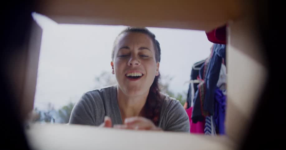 A young woman opens a cardboard box outdoors revealing a necklace she lifts it out with excitement her joy shining in the open air