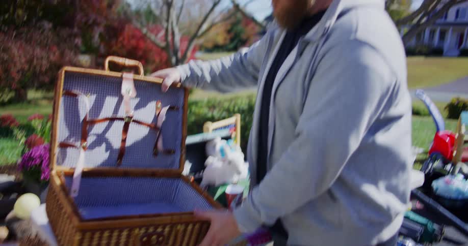 A man browses items at a yard sale in a suburban neighborhood under the open sky