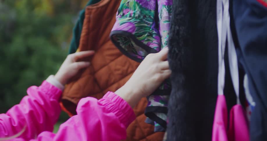 Hands browse through clothes hanging on a thrift sale rack outdoors