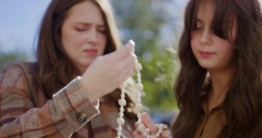 Two women hold and examine a white beaded necklace