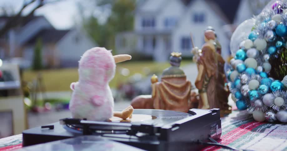 At an outdoor sale a whimsical pink stuffed bird spins in circles on a moving record player set on a table with other secondhand items