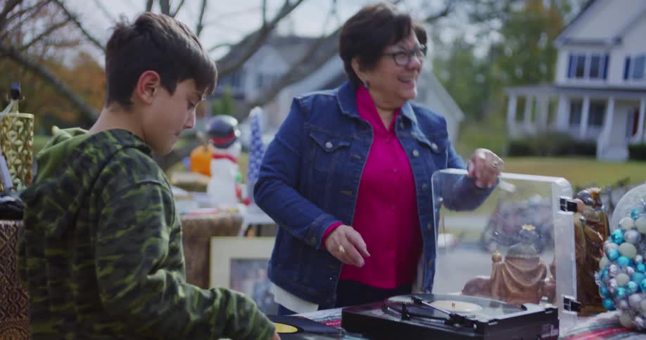 Grandmother and grandson dance while examining a record player at a yard sale on an autumn day