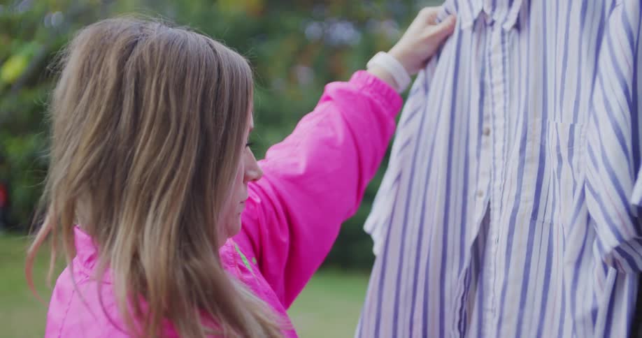 Young adult woman browsing hanged clothes outdoors during day time