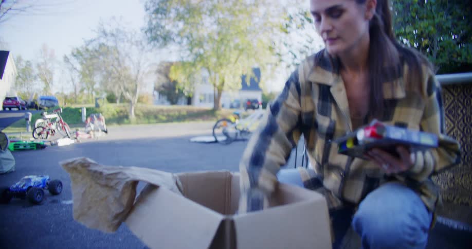 Young adult woman packing objects on a carboard box on the streets on a suburban area outdoors during day time