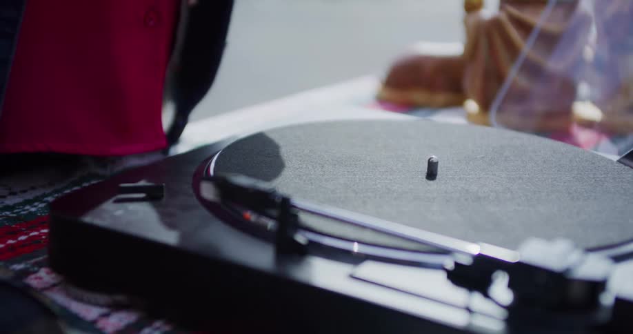 A close view shows a persons hands placing a vinyl record onto a turntable and gently lowering the needle onto the spinning record to play music