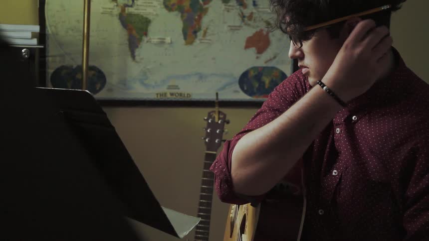 A man plays guitar and writes on some sheet music