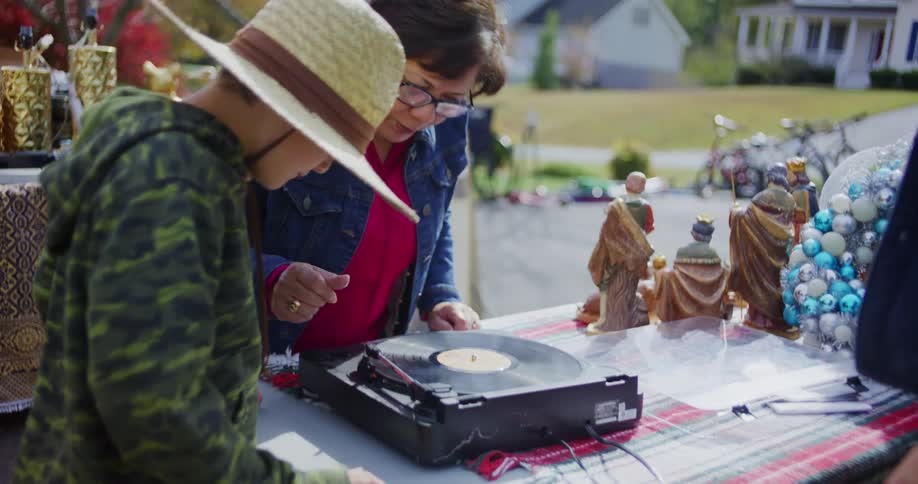 A woman and a young boy play a record and dance together at a garage sale