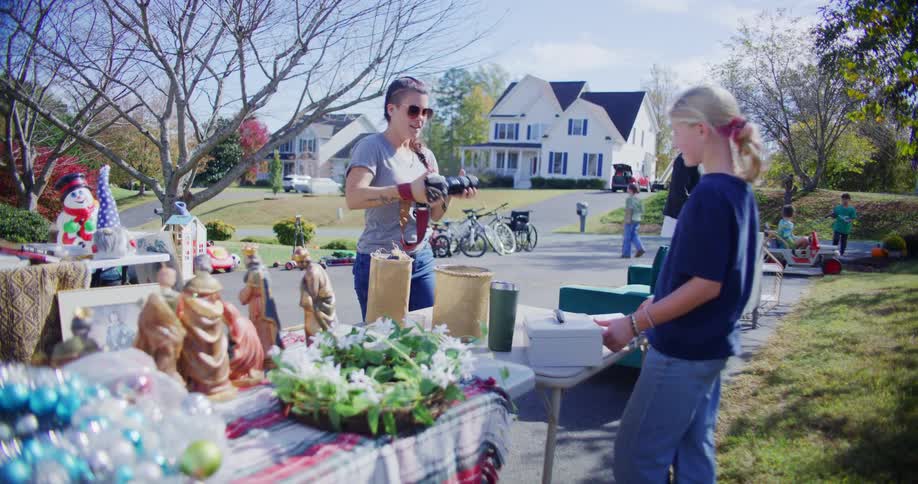 Woman holds a toy while talking to a child at an outdoor garage sale