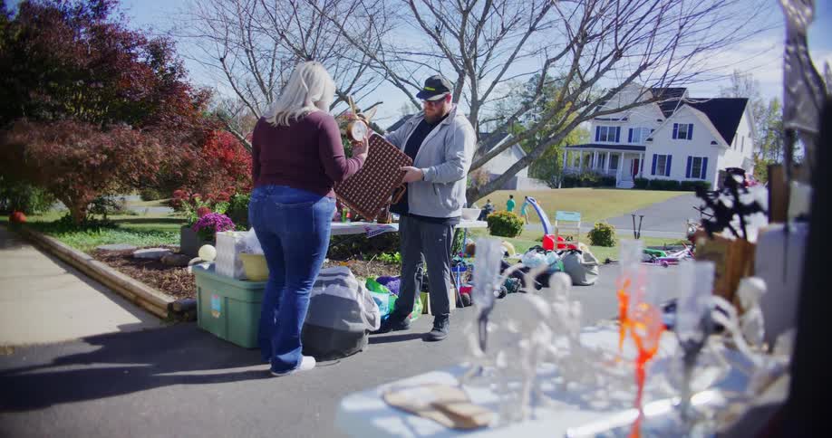 Two people examine used goods at a yard sale on an autumn day