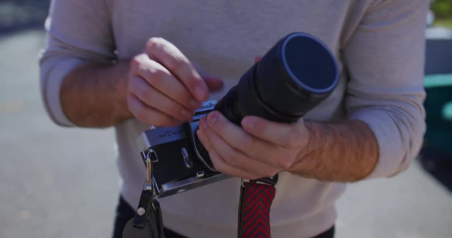 Young adult man setting up the parts of a camera and handling it to a young adult female standing next to him outdoors during day time