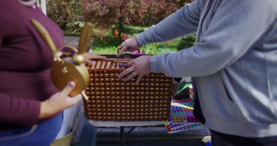 The man is standing closing a wooden basket that is on a table in an outdoor setting