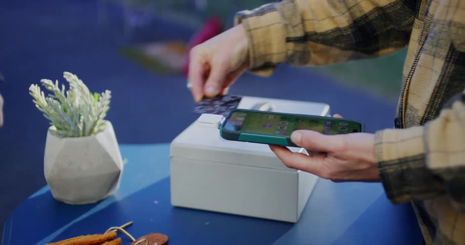 A person processes a mobile credit card payment for a customer at an outdoor vendor table