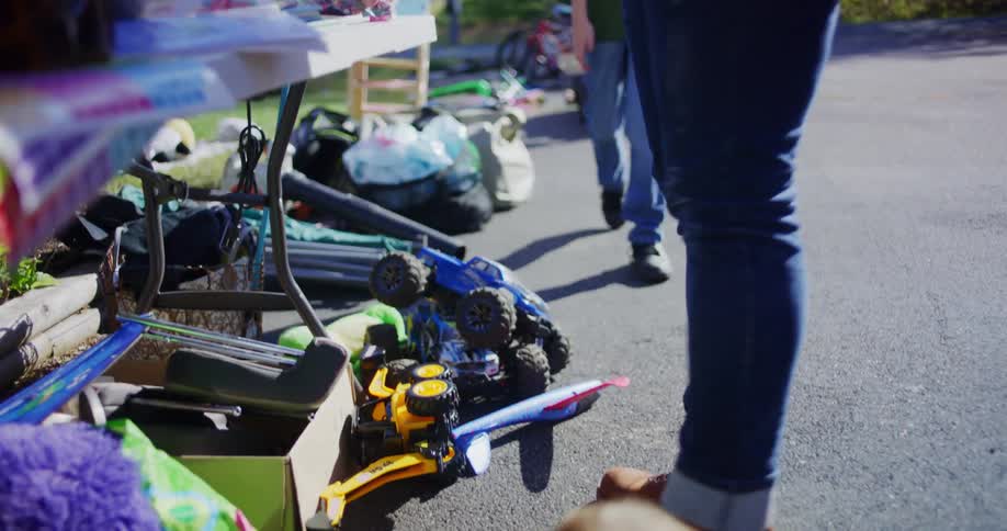 A father and son stand by a table as the son picks up a remote control car at a suburban yard sale