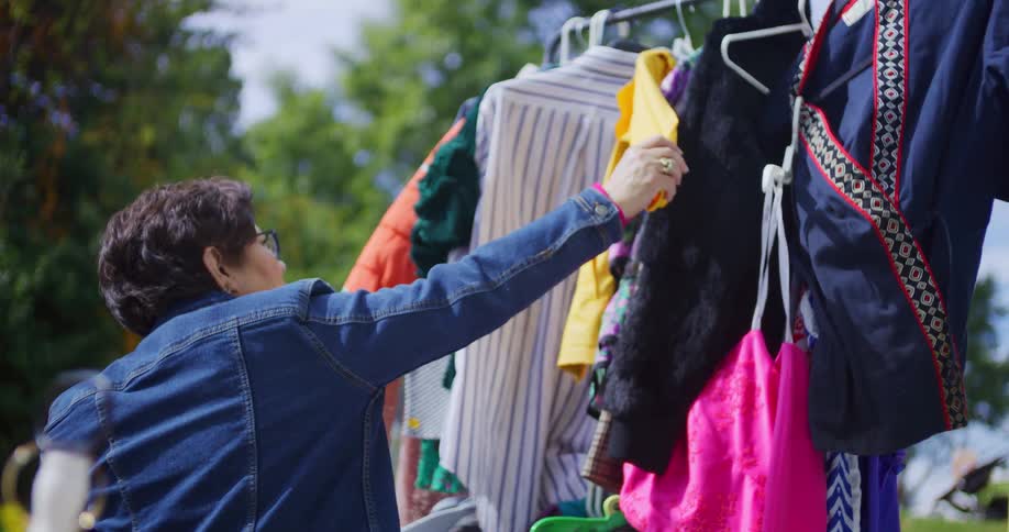 Woman examines shirt hanging on a clothing rack at an outdoor thrift sale