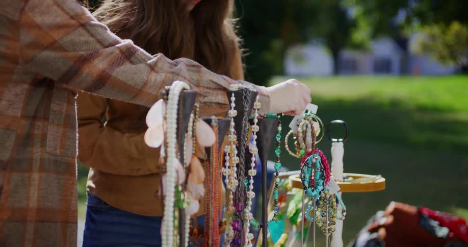 Two woman browse a display of colorful handmade jewelry at an outdoor market