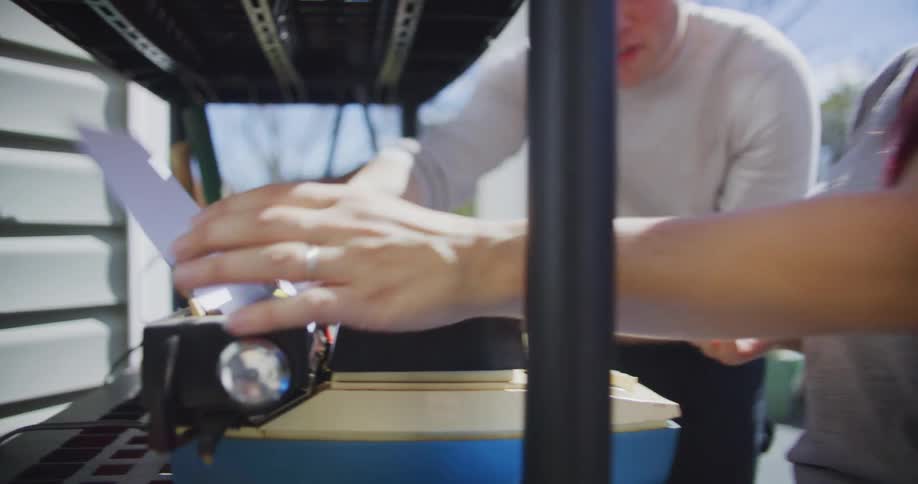 A close view of a woman operating a vintage typewriter on a black shelf while a man stands nearby both interacting with items at an outdoor yard sale