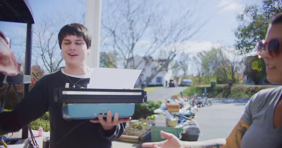 A man picks out a typewriter while talking to a woman at a suburban yard sale