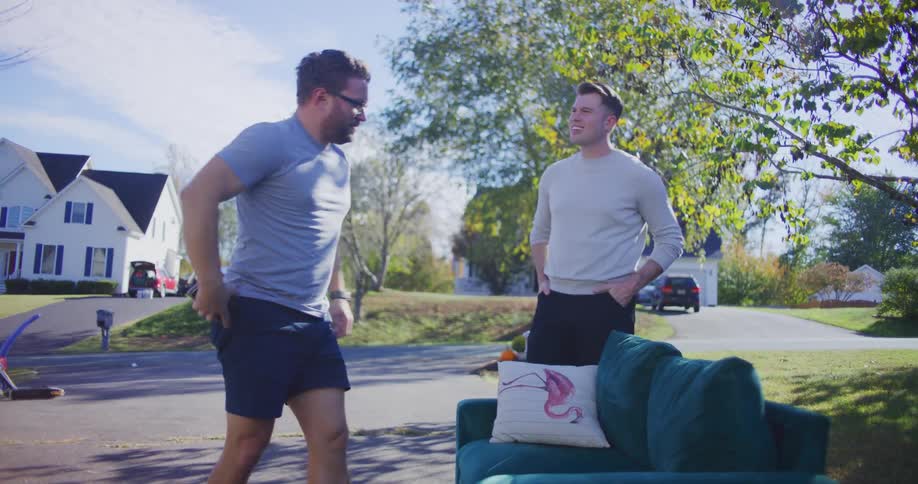 Two men examine a green sofa for sale in a suburban neighborhood at a yard sale
