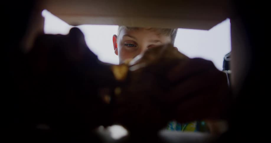 A young boy eagerly opens a cardboard box outdoors at midday his face lighting up as he pulls out a toy with excitement