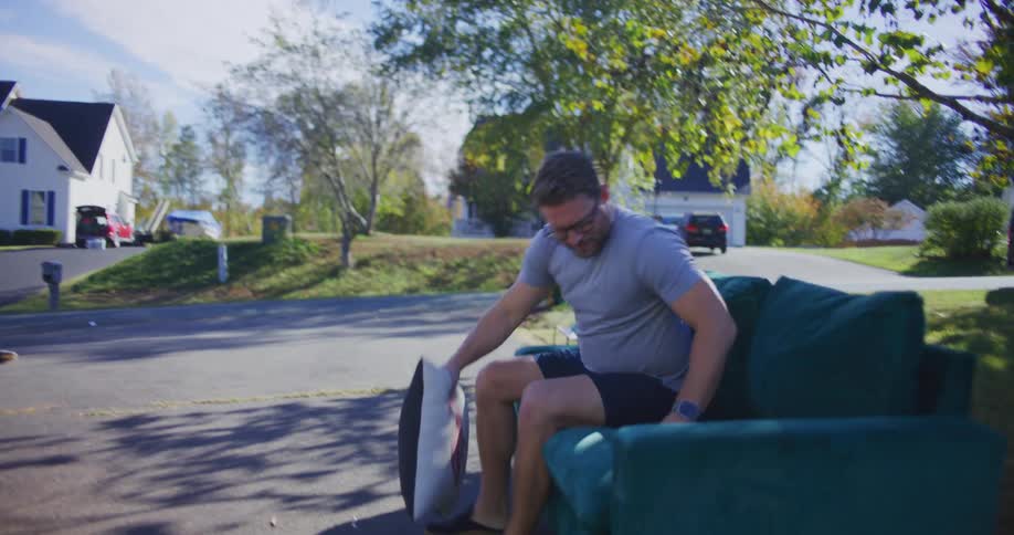 Man tests a couch placed on the driveway at a garage sale