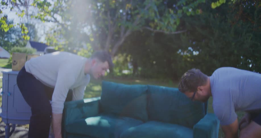 Two men shake hands before lifting and carrying a teal sofa together outdoors