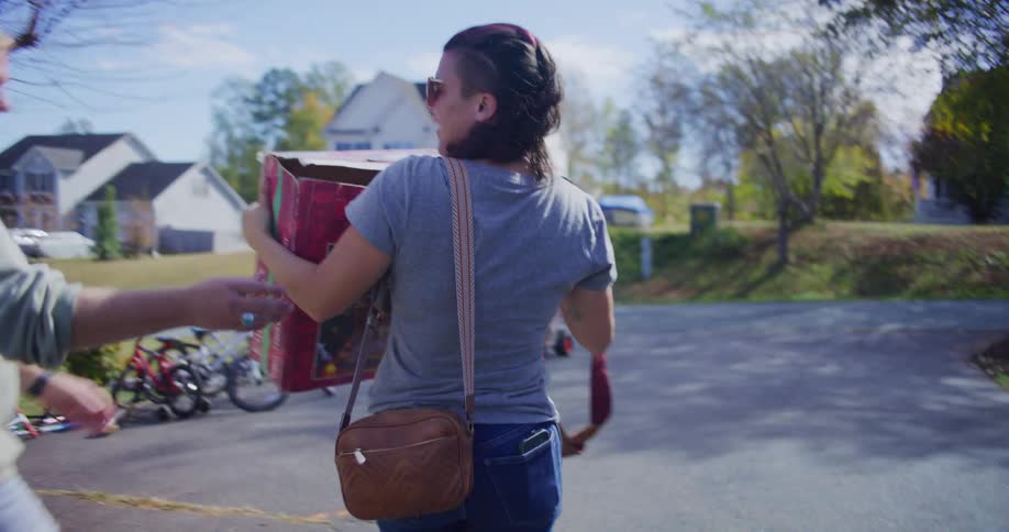Man helps a woman carry her purchases to her parked car during a yard sale on an autumn day