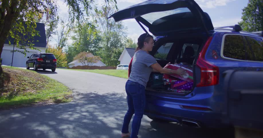 Woman watches man place bags and boxes in the trunk of a car