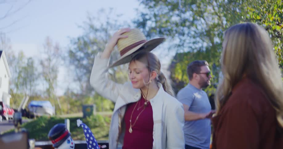 Two women pick out a straw hat together at a suburban yard sale