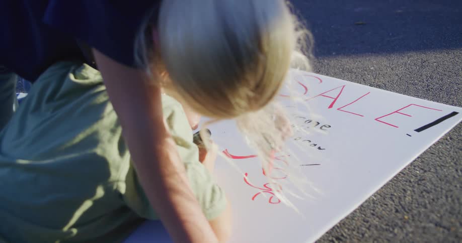 Children write a sale sign on a sheet placed on the ground