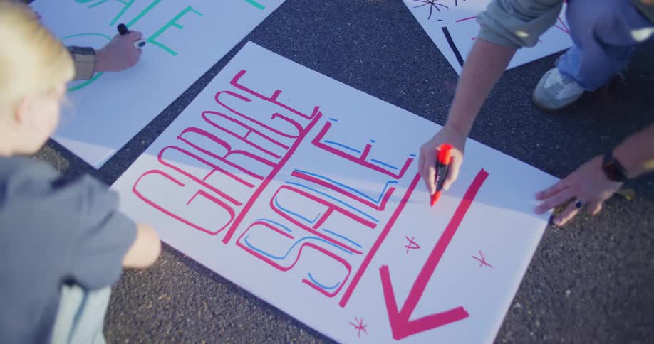 Children draw a garage sale sign with arrows and colorful letters on the ground