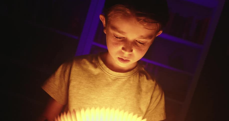 Boy holding an illuminated open book in a dark room