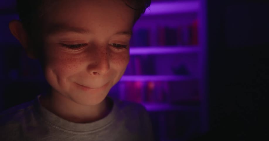 Child holds a phone lighting up their face in a dark room