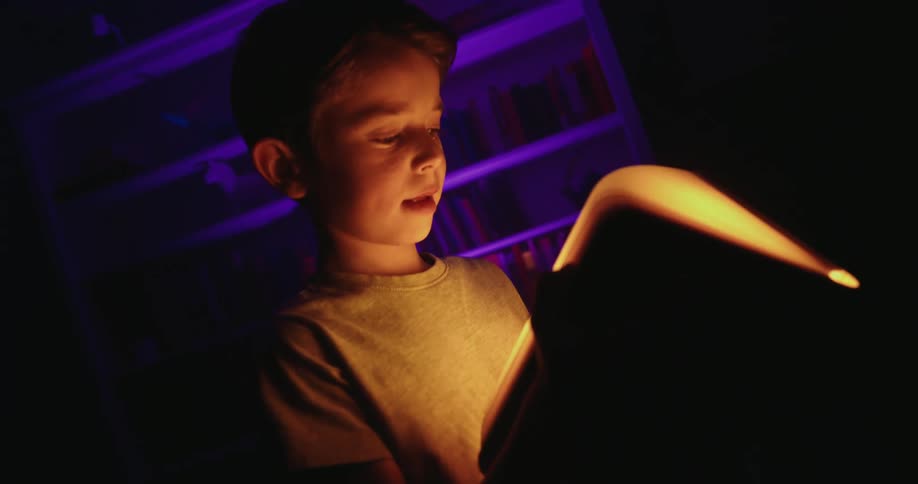 Child holds a glowing book in a dark room
