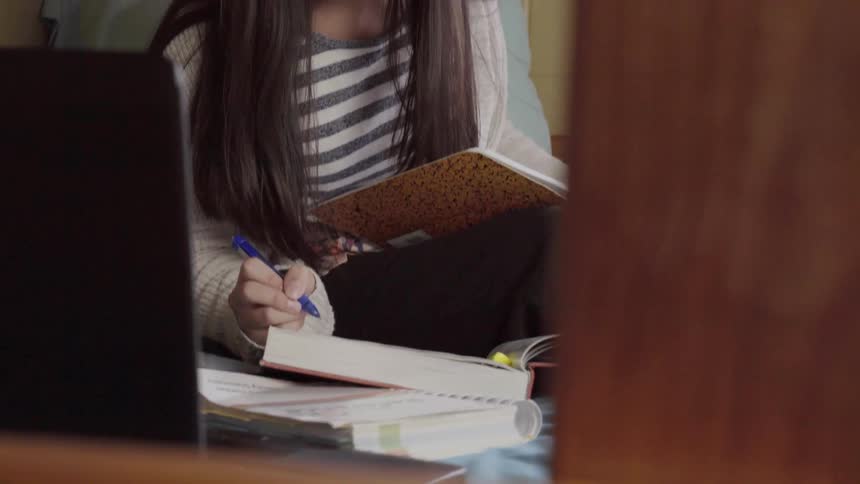 A woman highlights a textbook while sitting on a bunk bed