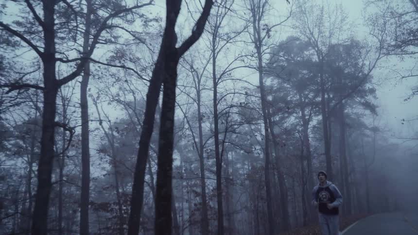 A man runs on a road alongside a forest on a cloudy afternoon in the fall