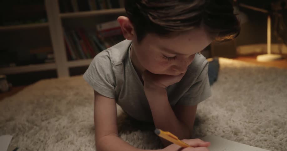 Young student lies on the rug while working on his homework
