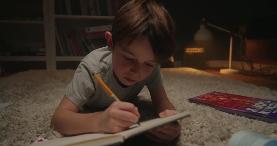 Child writes in a notebook while books and papers are scattered across the rug