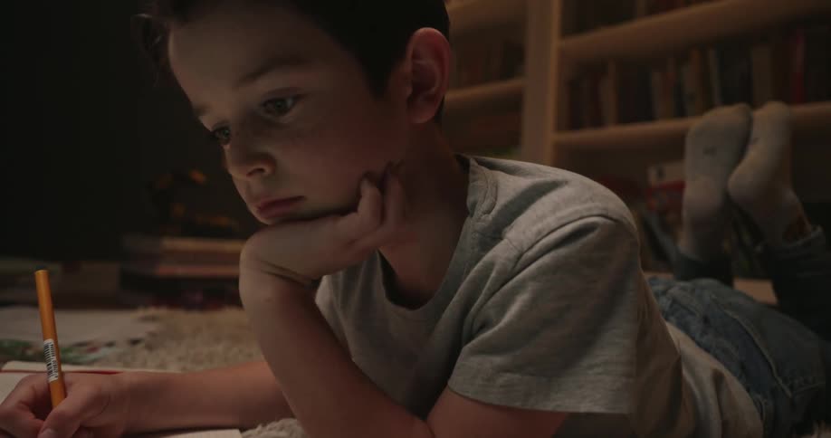 A young boy lays on his stomach while looking at his tablet computer