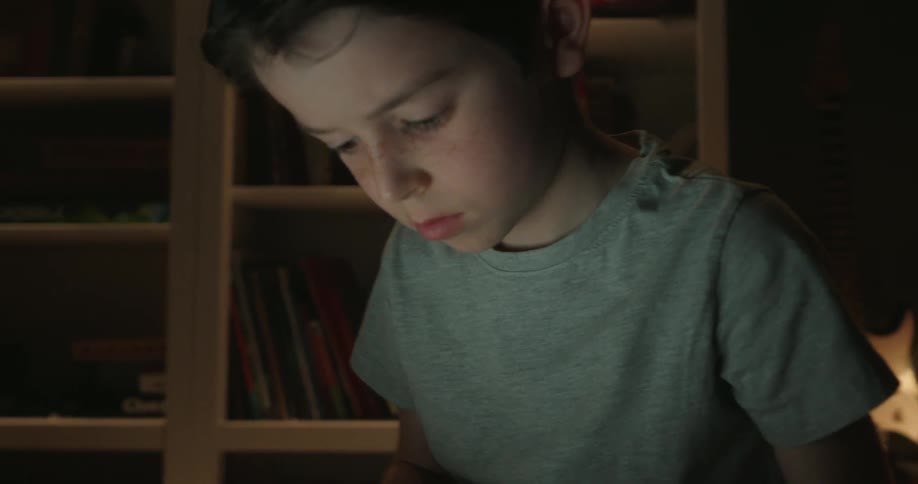 Child uses a laptop while sitting on the floor of a softly lit bedroom