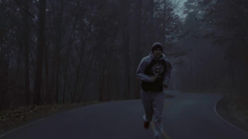 A man jogs down a road lined with trees on a foggy night