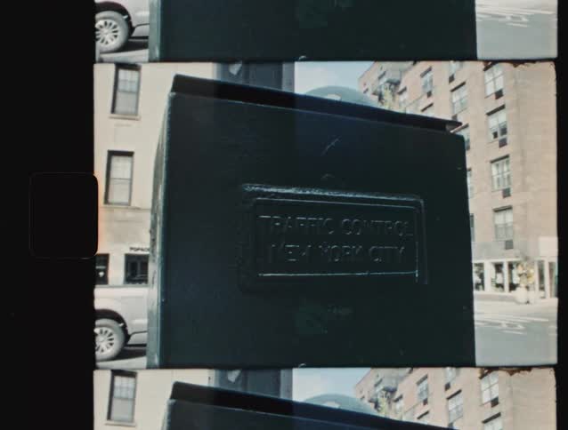A close view of a dark metal street control box with a raised sign reading new york city filmed on 16mm film stock with apartment buildings visible in the background