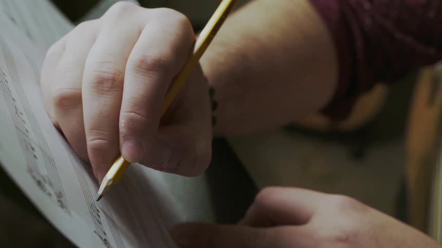A man is writing with a pencil on sheet music