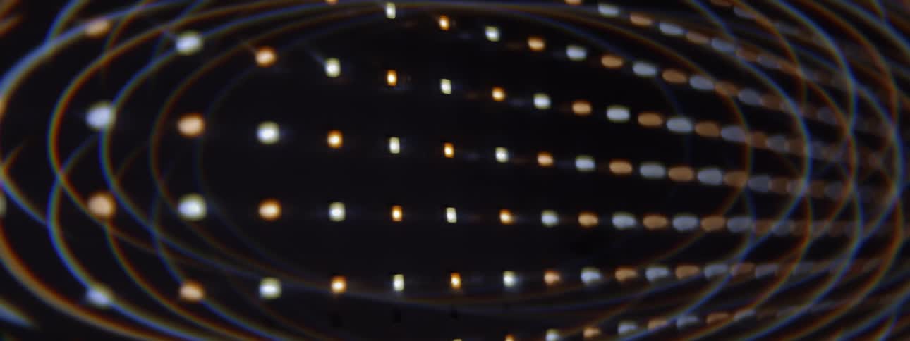 The clip shows a dynamic abstract visual effect featuring rows of small glowing lightssome whitecool some orangewarmon a black background the lights appear to be moving or rotating creating a strong sense of threedimensionality and curvature po
