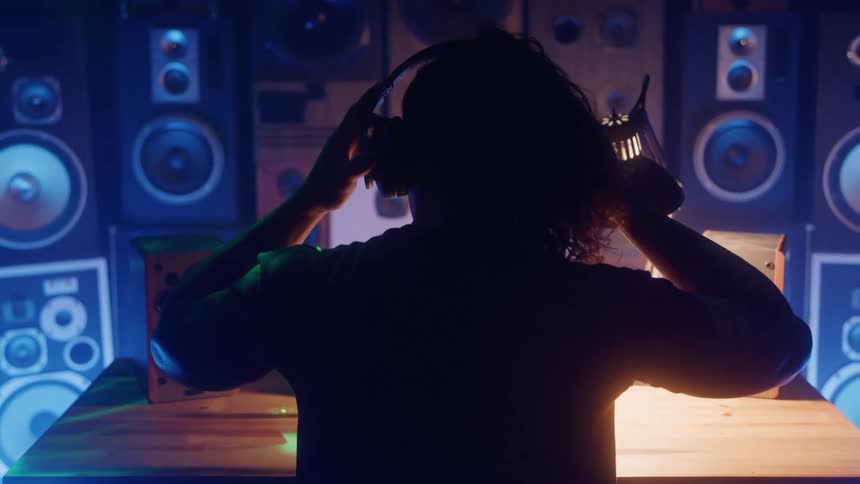 Man sitting in a dimly lit room containing many speakers puts on headphones