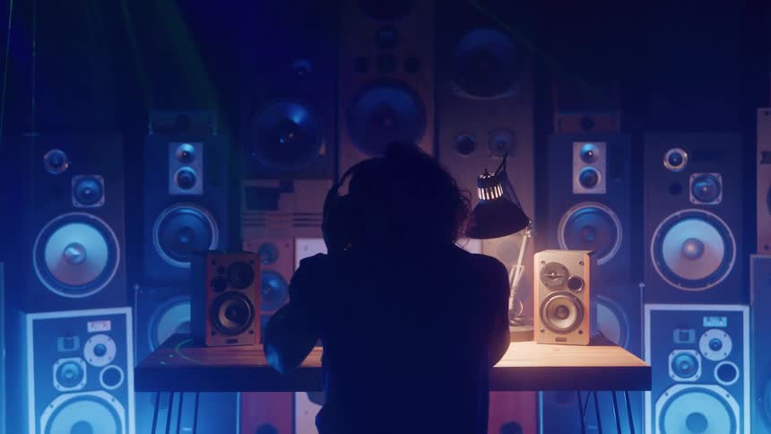 Man bounces in his seat while listening to music in a room containing a wall of speakers