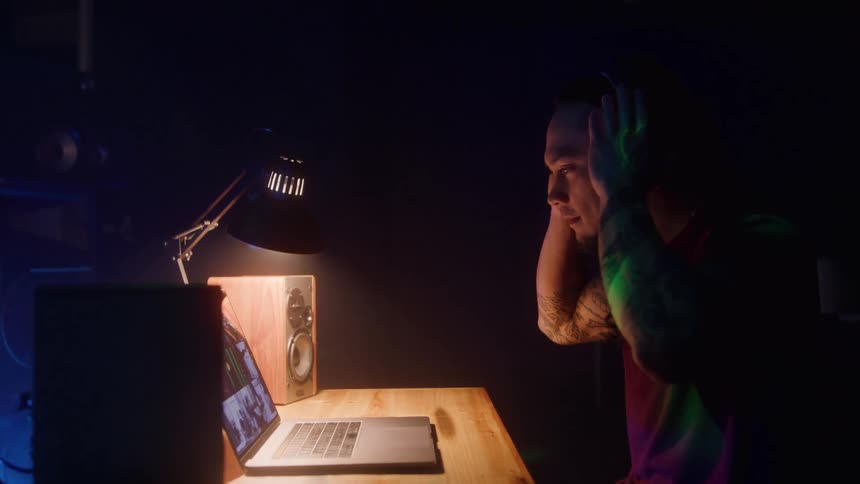 Young man sits at a desk in front of his laptop computer as he puts on headphones