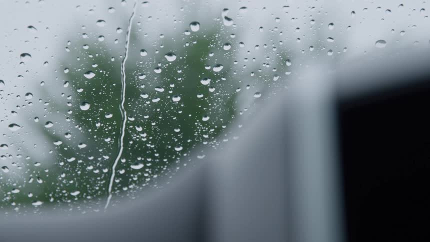 The video features a closeup static shot of a window covered in raindrops suggesting it is rainingwater droplets of various sizes cling to the glass with several streaks of water running vertically down the surface over the course of the clipthe