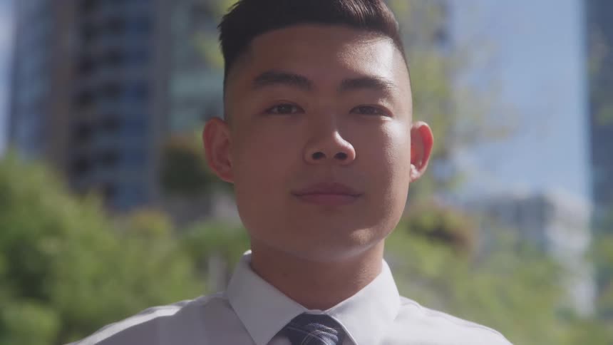 Young man standing in the downtown sun turns his head and smiles